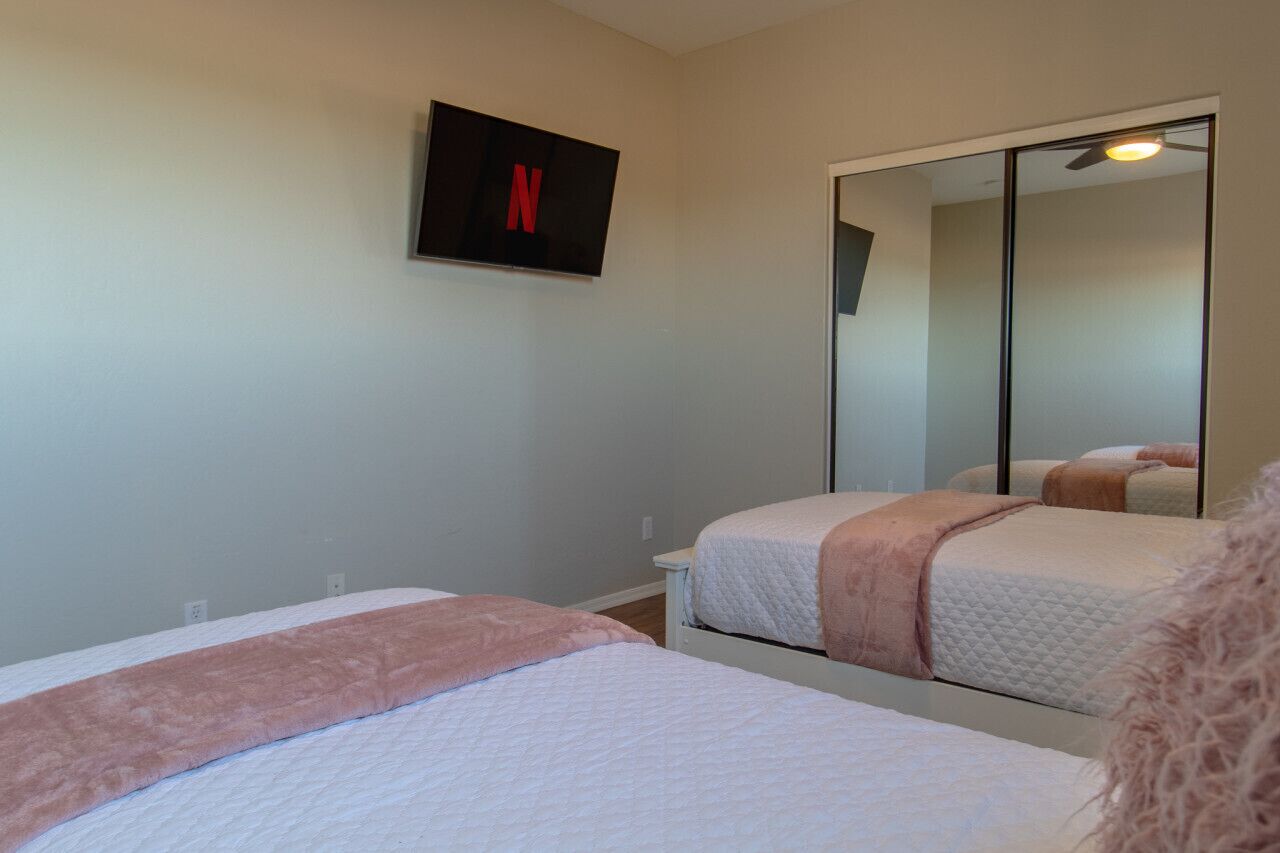 Une chambre avec deux lits, un grand miroir et un téléviseur fixé au mur qui affiche le logo de Netflix.