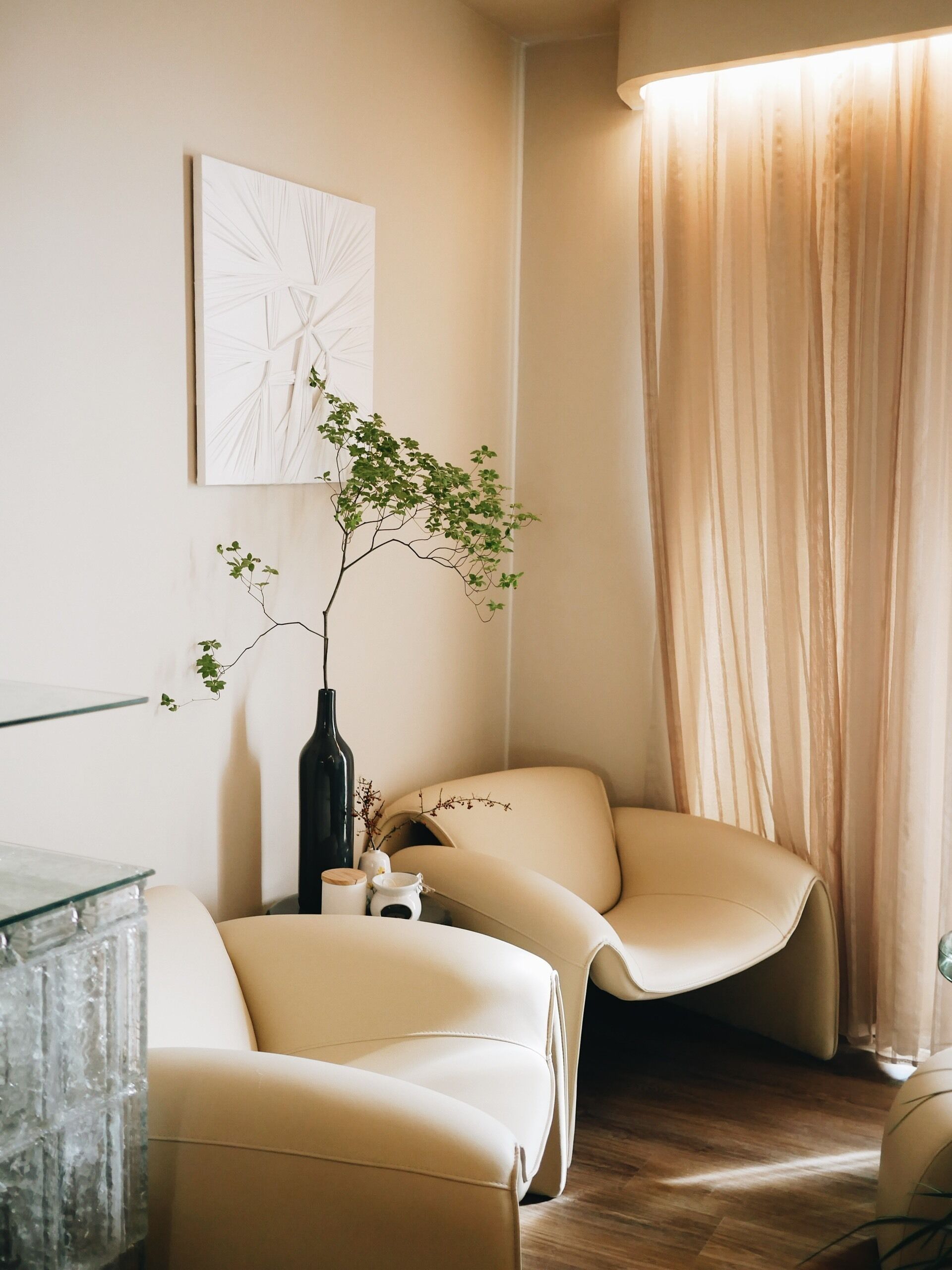 Een moderne woonkamer met een glazen salontafel, een beige bank en een bijzettafeltje met decoratieve spullen.