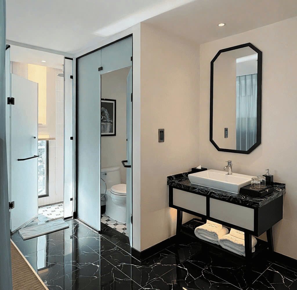 Un bagno moderno con un mobile lavabo bianco e nero, uno specchio grande e un water visibile attraverso una porta in vetro.