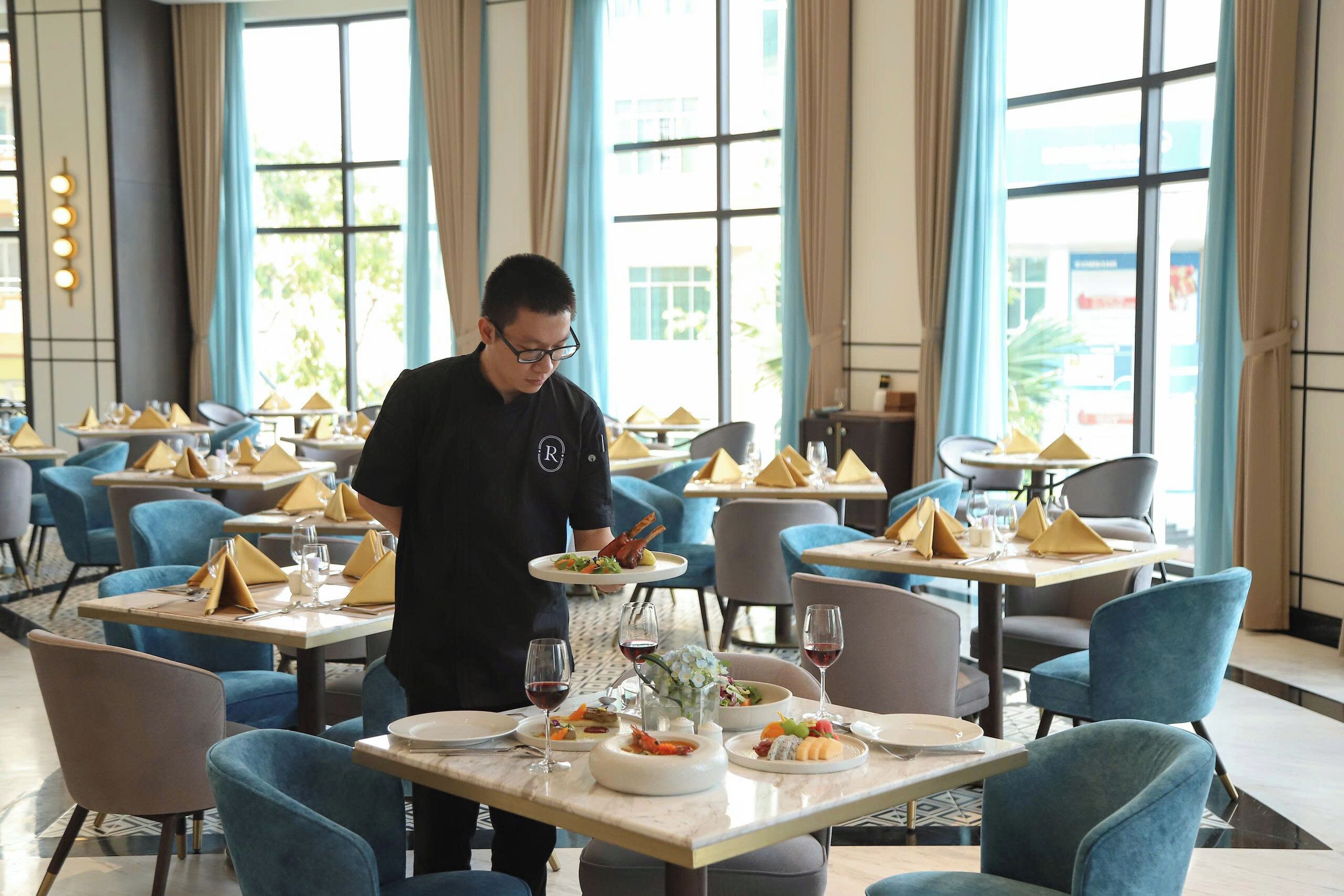 A restaurant with tables set with blue chairs, white plates, and wine glasses.