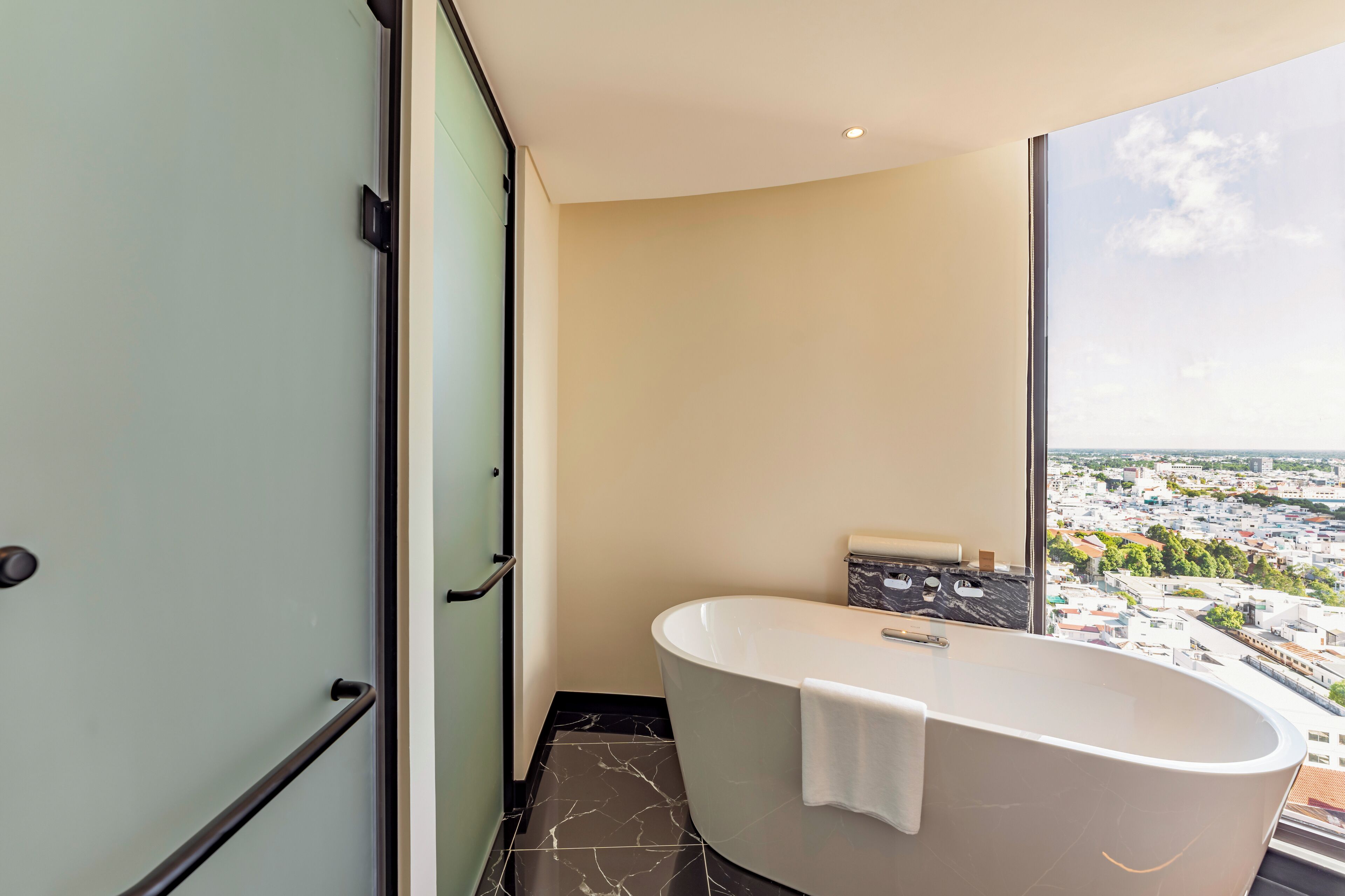 A modern bathroom with a freestanding bathtub, a glass shower enclosure, and a large window offering a city view.