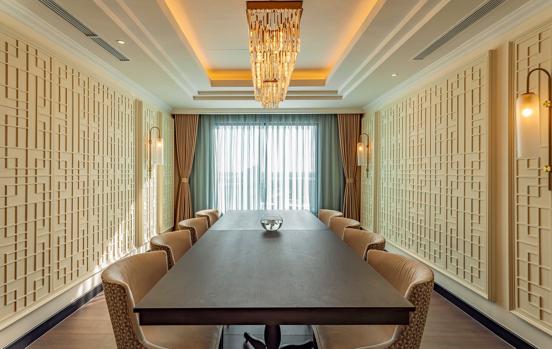 A conference room with a long table, leather chairs, a chandelier, and patterned walls.