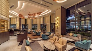 A modern hotel lobby with a mix of seating areas, a bar, and large windows offering city views.