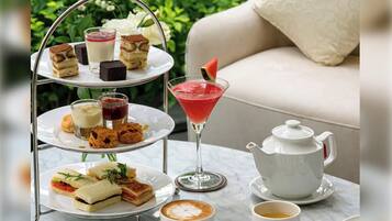 A three-tiered dessert stand with various pastries, a martini glass with a fruit garnish, a teapot, and a cup of coffee on a table.