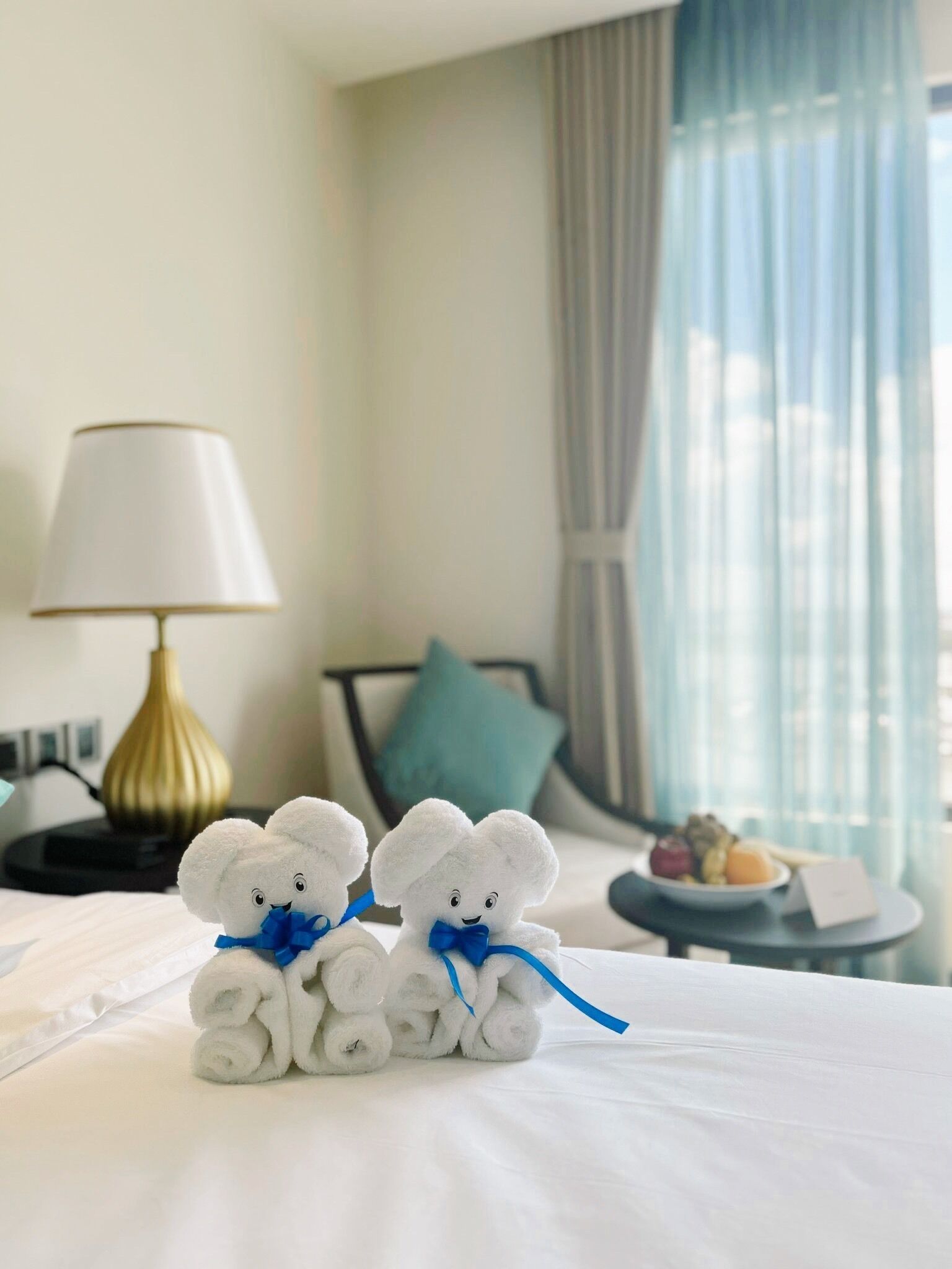 Una habitación de hotel con una cama, una lámpara y una pequeña mesa con frutas.