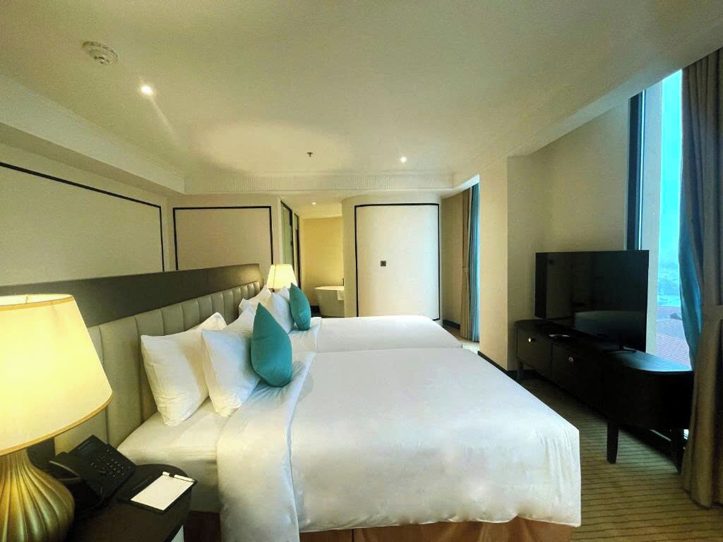 A hotel room with a large bed, a desk with a lamp, a television, and a view of the outdoors.
