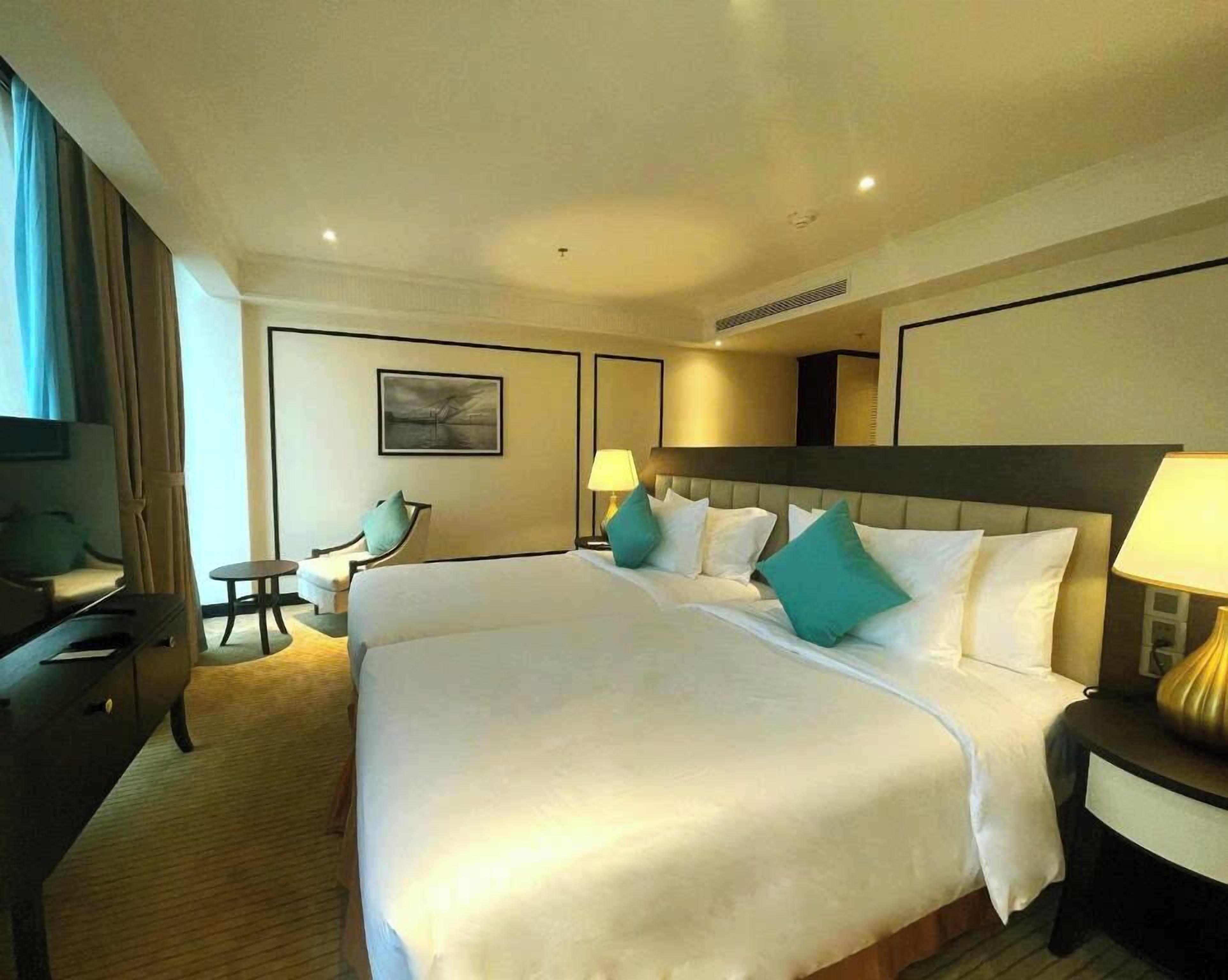 A hotel room with a large bed, two bedside tables with lamps, a chair, a small table, and a painting on the wall.