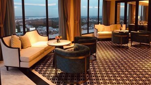 A modern hotel room with a large window offering a city view, a patterned floor, and a seating area with a sofa and armchairs.
