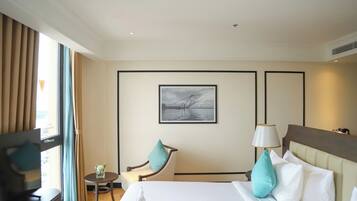Habitación de hotel con cama, una silla, una mesita, una lámpara y un cuadro en la pared.