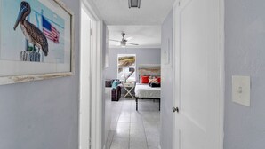 A hallway leading to a bedroom with a bed, a ceiling fan, and a painting of a pelican. - The Cozy Pelican Studio! Just Steps to the Sand! (Hollywood)