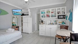 A compact hotel room with a bed, a desk, a kitchenette, and a TV. - The Cozy Pelican Studio! Just Steps to the Sand! (Hollywood)