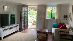 A living room with a TV, sofa, and a door leading to a garden. - Beautiful Blue Mountains Garden Flat
 (Katoomba)