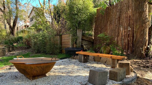 A rustic outdoor area with a large metal basin, wooden benches, and a stone wall. - Beautiful Blue Mountains Garden Flat
 (Katoomba)