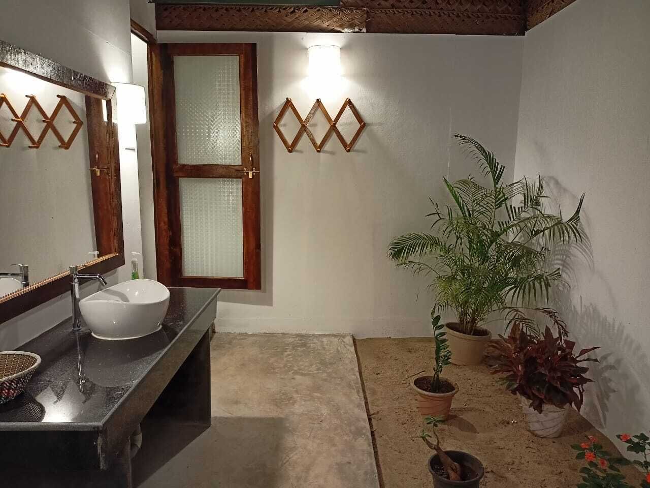 A bathroom with a white sink, a mirror, a wooden-framed window, and decorative wall lights.