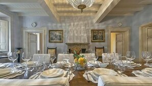 Un comedor formal con una larga mesa dispuesta para una comida, flanqueada por sillas, y una chimenea en el centro.