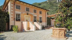 Un edificio de dos pisos con fachada color beige, una entrada central con escaleras y una fuente de piedra al frente.