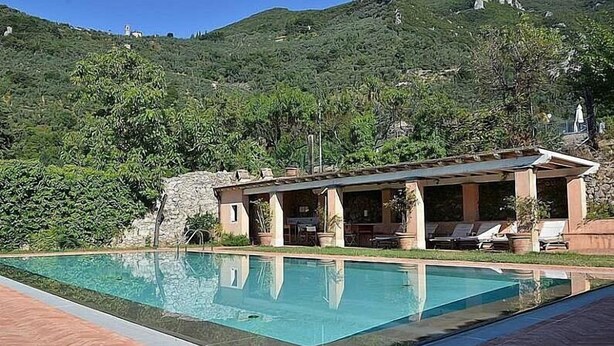 Zona junto a la piscina con piscina, sillones de descanso y un edificio de fachada de piedra.