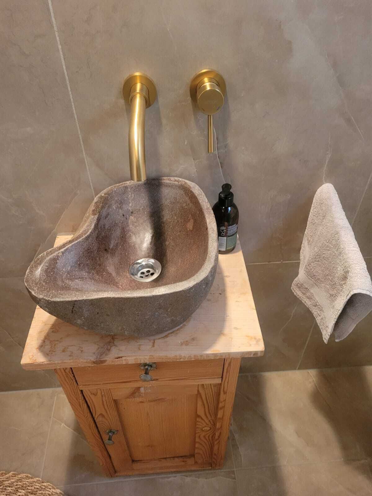 Een badkamermeubel met een wasbak van natuursteen, messing details en een houten kastje eronder.
