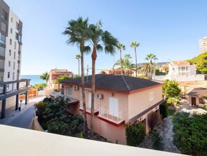 Un edificio residencial con techo rojo, barandillas blancas en el balcón y palmeras al fondo.