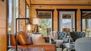 Interior acogedor de una cabaña con un sofá de cuero, una mesa con lámpara y dos sillones tapizados.