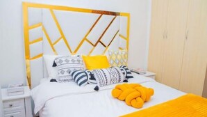 Een bed met een hoofdbord in wit en geel, meerdere kussens en een gele deken.