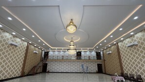 Un hallo espacioso con techo alto, un candelabro central y una zona de escenario con una mesa y sillas.