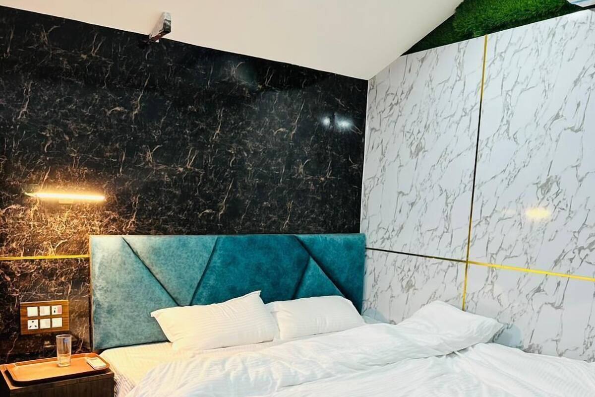 Quarto moderno com parede em padrão marmorizado, cabeceira estofada em tom de azul-esverdeado e cama bem arrumada com lençóis brancos.