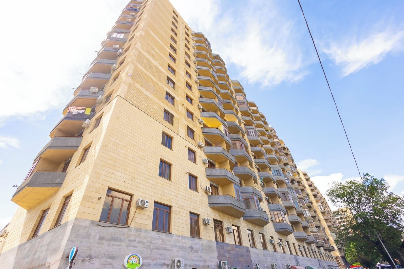 A high-rise residential building with multiple balconies, air conditioning units, and a clear sky.
