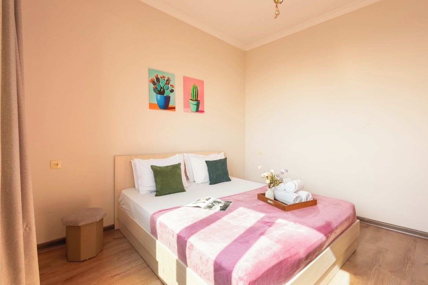A bedroom with a bed, pillows, a bedside table, a trash bin, and two wall-mounted paintings.