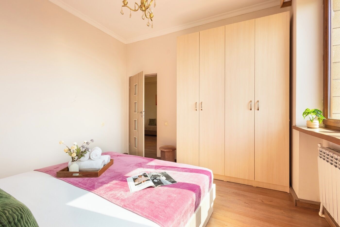 Une chambre à coucher avec un lit, une table de chevet ornée d’un vase et de serviettes, une armoire et une fenêtre avec une plante.