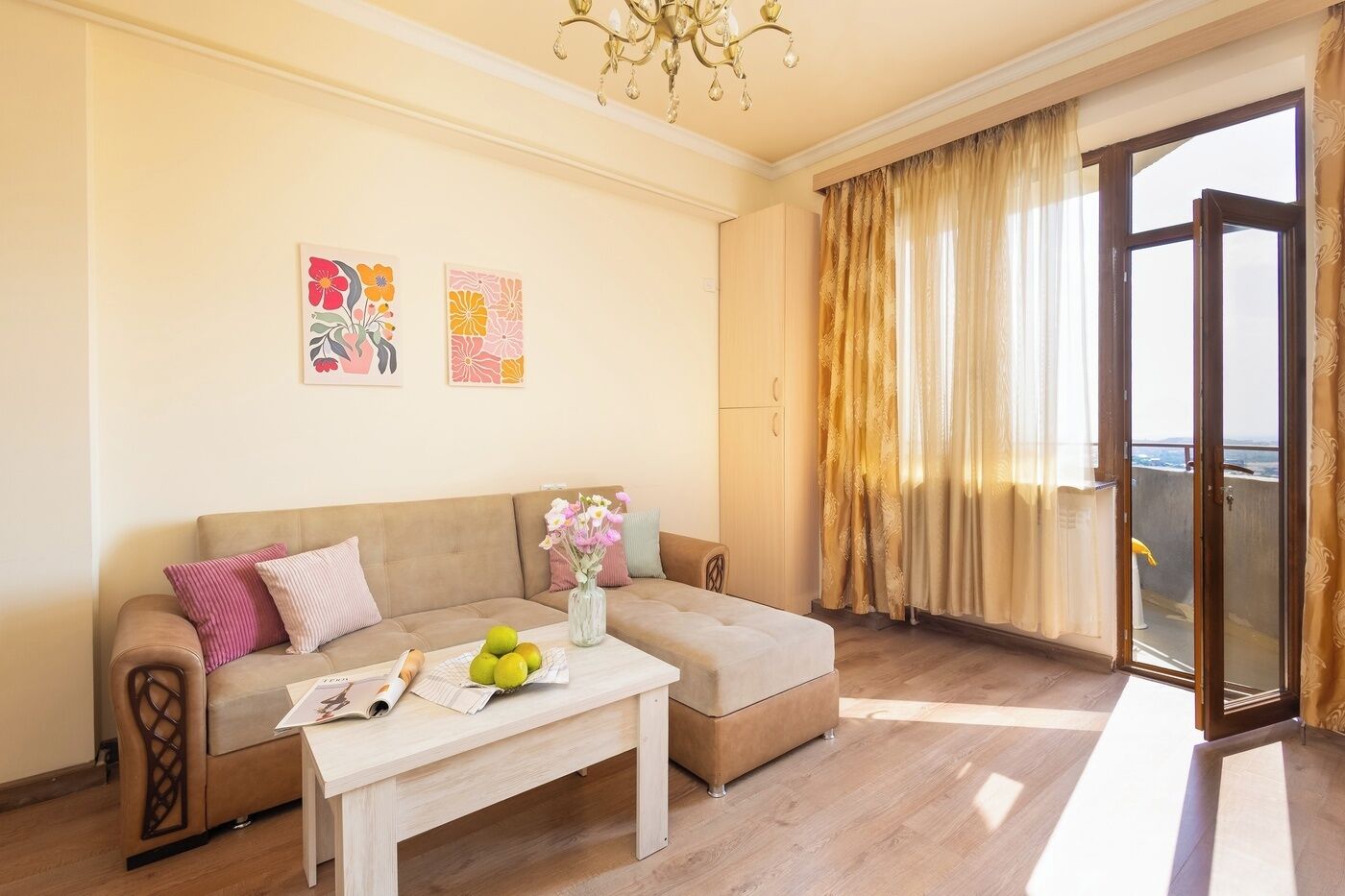 A living room with a sofa, a coffee table with fruit and a magazine, a chandelier, and a sliding glass door to the outside.