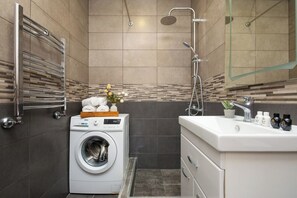 Ein modernes Badezimmer mit Waschmaschine, Dusche und Waschtisch mit Toilettenartikeln.