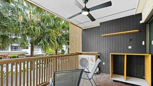 A covered outdoor area with a ceiling fan, a wooden railing, and a seating area with a chair.