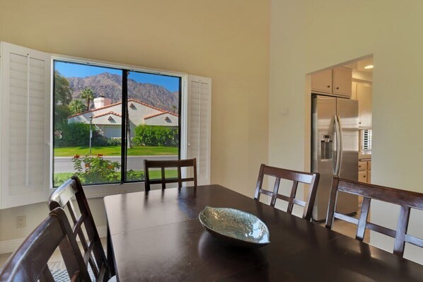 A dining area with a table and chairs, a view of a mountain and greenery, and a kitchen with appliances.