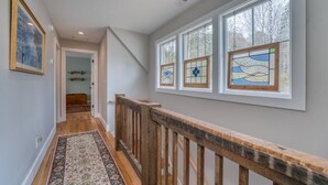 Un couloir doté d’un plancher en bois, d’un tapis à motifs et d’une rambarde en bois.