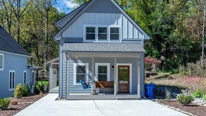 Une maison à deux étages avec un porche à l’avant, une chaise suspendue et une porte dotée d’une fenêtre.