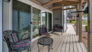 Une véranda couverte avec un plancher en bois, deux fauteuils rembourrés, une petite table et une porte-fenêtre coulissante donnant sur la maison.