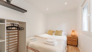 Un dormitorio con cama, mesita de noche, lámpara de noche, armario y ventana.