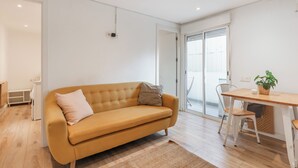 Una sala moderna con un sofá, una mesa de comedor y una silla. Hay un ventanal corredero que da a un balcón.