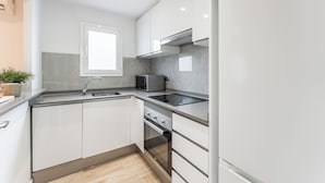 Una cocina moderna con gabinetes blancos, horno empotrado, microondas y lavamanos.
