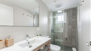 Un baño moderno con un espejo grande, un lavamanos doble, un inodoro y una ducha con mampara de vidrio.