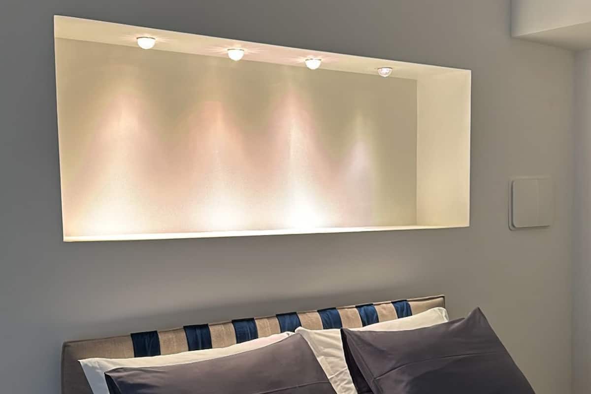 A modern bedroom with a large bed, a headboard with built-in lighting, and a wall-mounted light fixture above the bed.