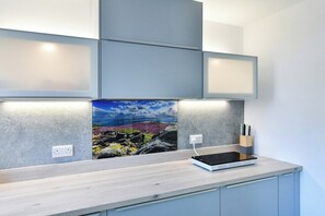 A modern kitchen with a built-in stove, a tablet on the counter, and a painting of a landscape. - 4Bed House Near Nottingham (Clifton)