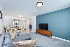 A modern living room with a grey sofa, a wooden TV stand, and a blue accent wall. - 4Bed House Near Nottingham (Clifton)
