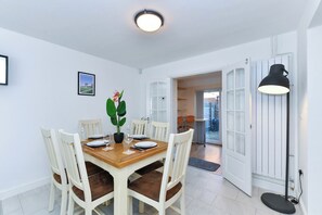 En matplats med ett träbord, vita stolar, en krukväxt och en svart golvlampa.