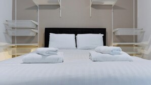 Ett hotellrum med en säng, två vita handdukar, en svart sänggavel och vita hyllsystem.