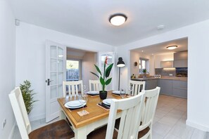 A dining area with a wooden table, white chairs, and a potted plant. - 4Bed House Near Nottingham (Clifton)