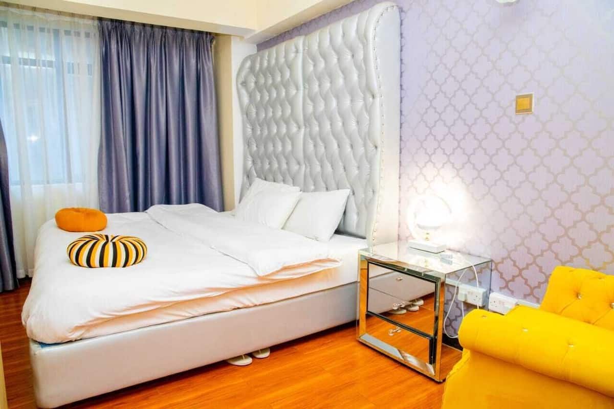 A neatly made bed with white linens and two pillows, a bedside table with a lamp, and a bright yellow armchair.