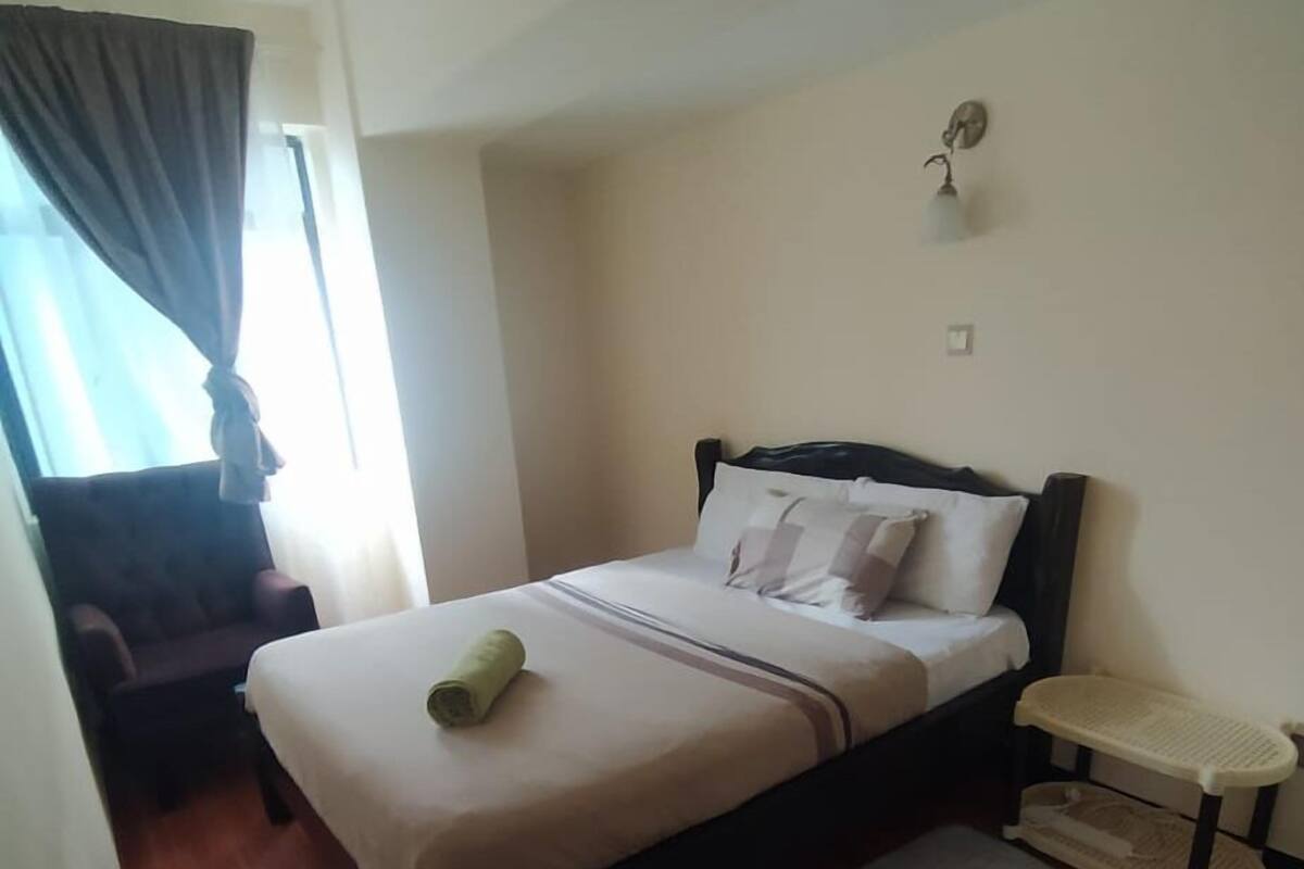A bedroom with a bed, a nightstand, a chair, a window with curtains, and a wooden floor.