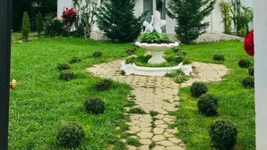 Un edificio blanco con techo rojo, un jardín central con fuente y un camino pavimentado.